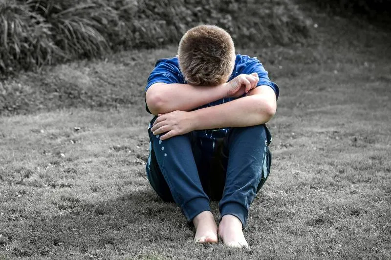 Un adolescent assis dans l'herbe, la tête posée sur les genoux.